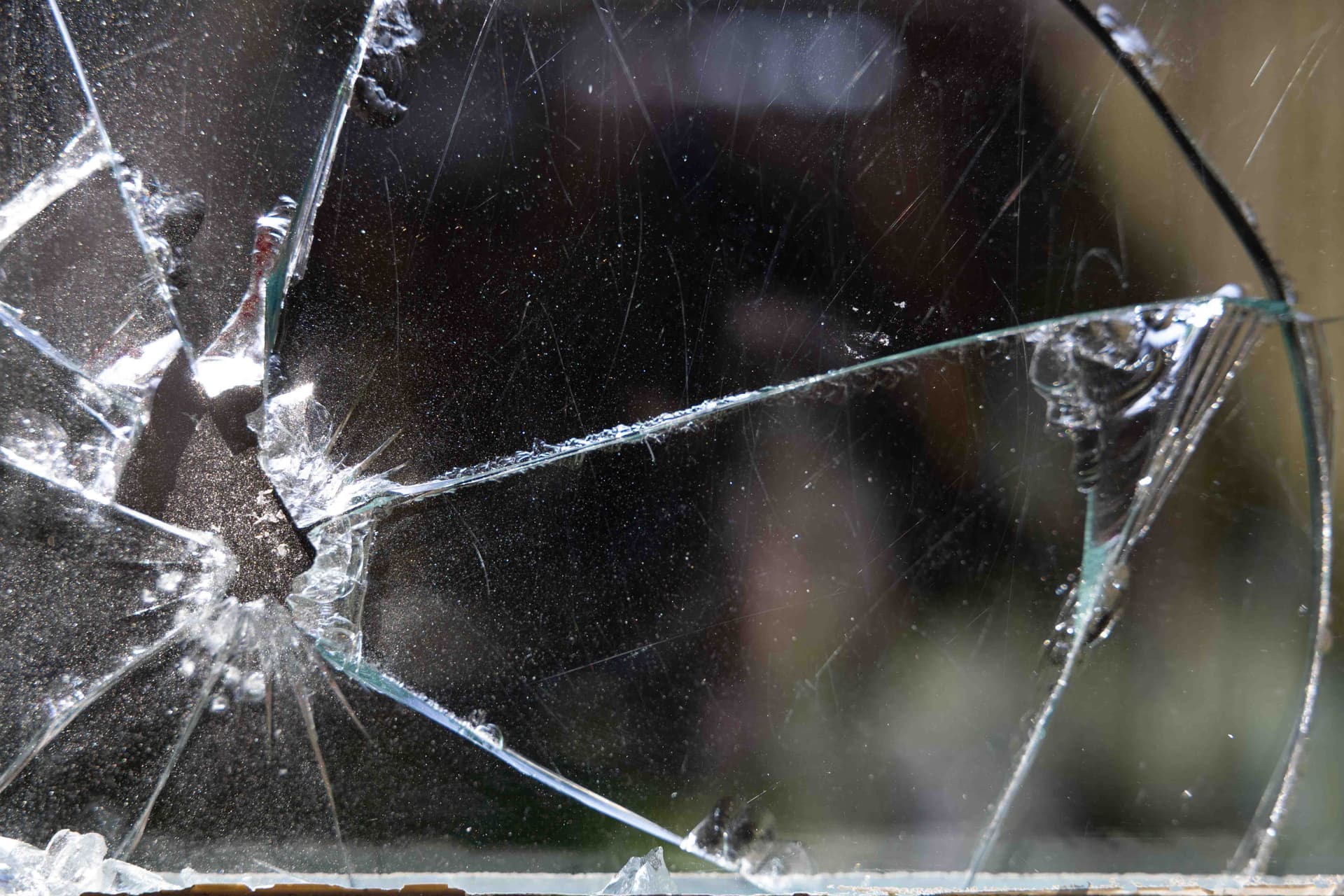 Close-up van een gebroken ruit met een duidelijk inslagpunt en scheuren in het glas.