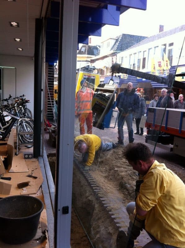 Glaszetters plaatsen met behulp van een kraan een lastig bereikbare ruit. Om de ruit veilig te kunnen plaatsen, is de straat opengebroken en is een deel van het beton verwijderd.